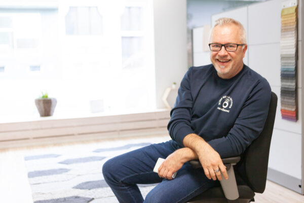 Neurosonicin kehittäjä Marco Kärkkäinen hymyilee toimistotuolissa Neurosonic-paidassa.